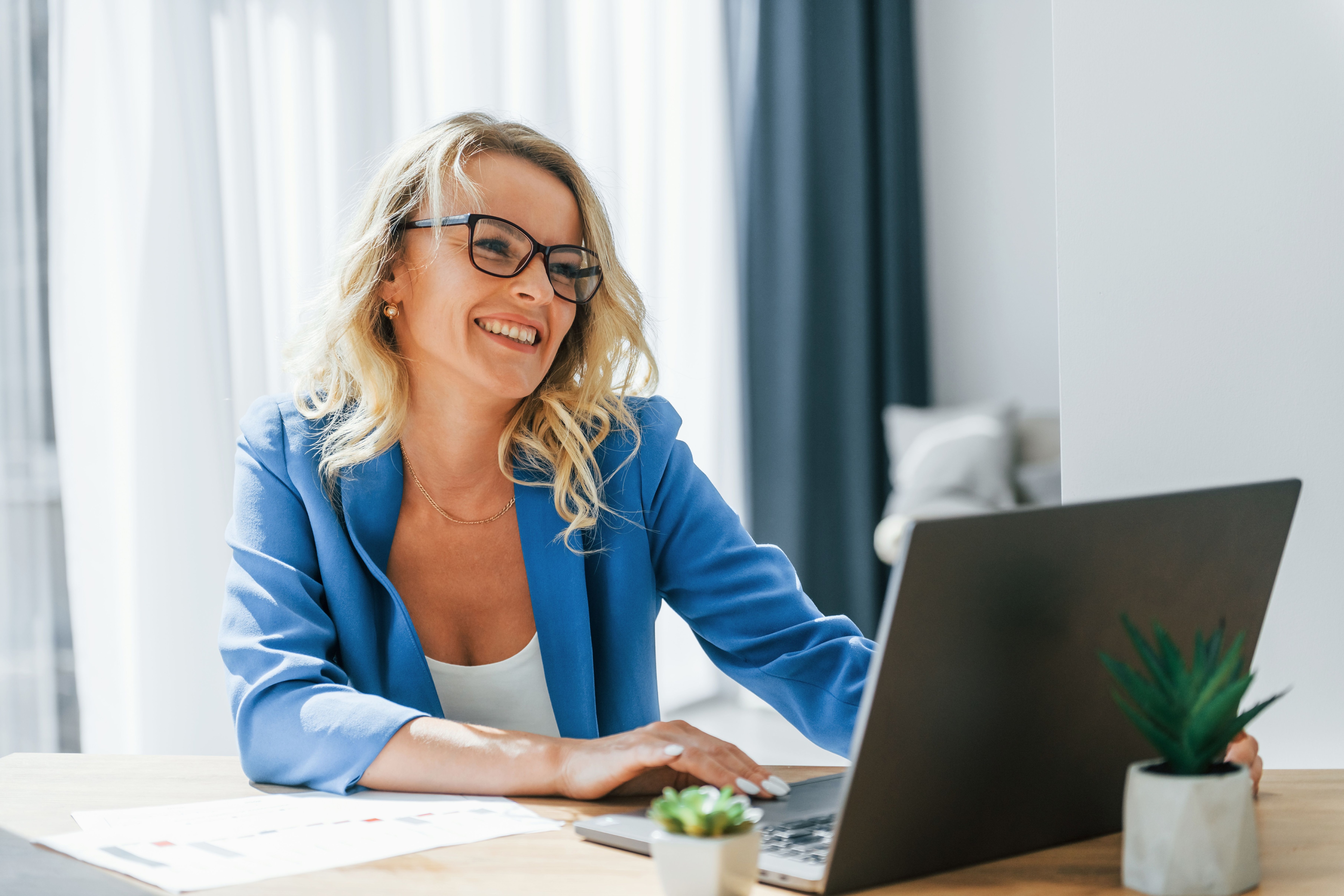 Smiling blonde woman with glasses working on a laptop in a blue blazer.jpeg