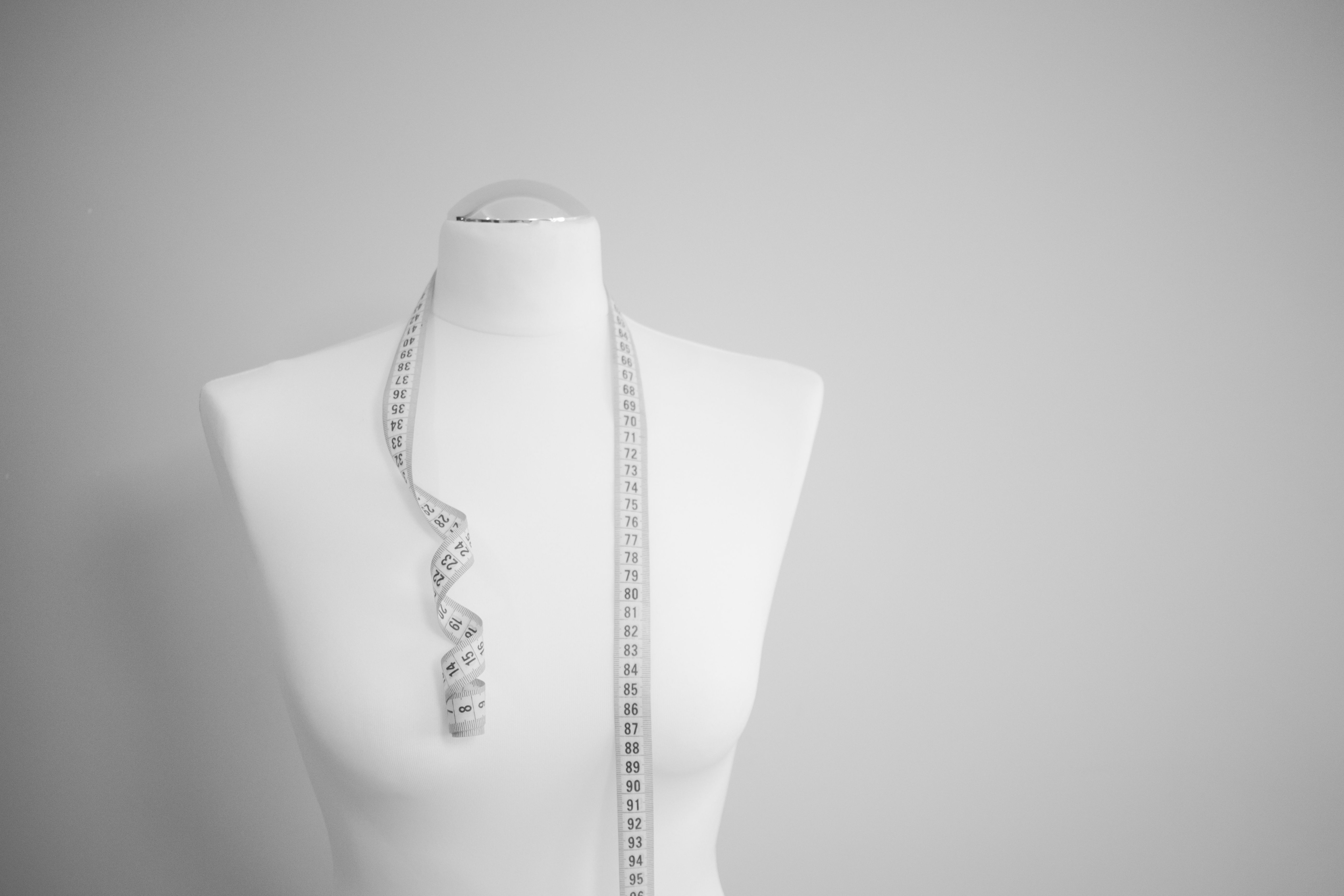A white mannequin torso with a measuring tape draped around the neck.jpeg